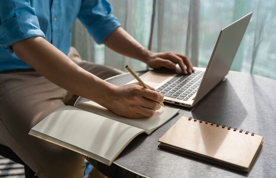 Someone writing on a notepad in front of a computer