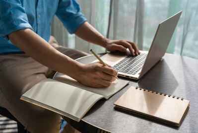 Someone writing on a notepad in front of a computer