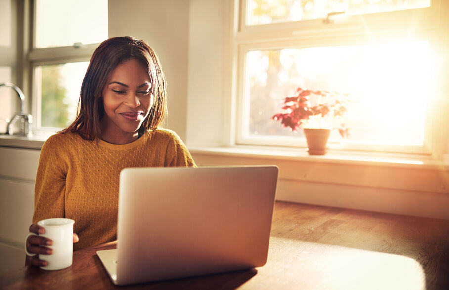 A woman sitting on a laptop by a sunny window