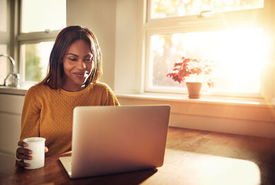 A woman sitting on a laptop by a sunny window