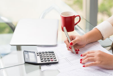 Someone holding a calculator over a contract with a small house in the background