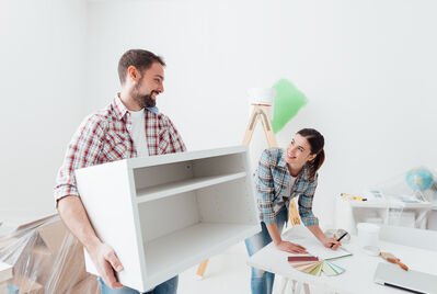 One person carrying a cabinet while another person writes something in a notepad