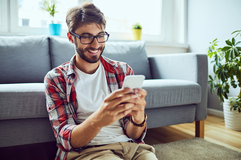 Smiling young man sitting on floor checking online account