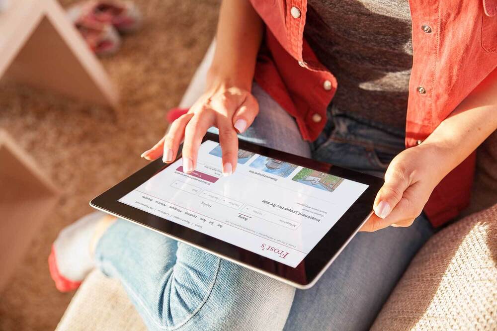 Lady looking at investment properties on tablet sat on sofa