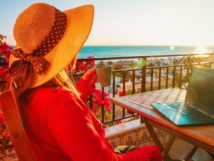 Woman sitting on a sunny balcony in front of a laptop