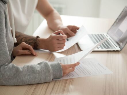 Two people holding some paper in front of a laptop