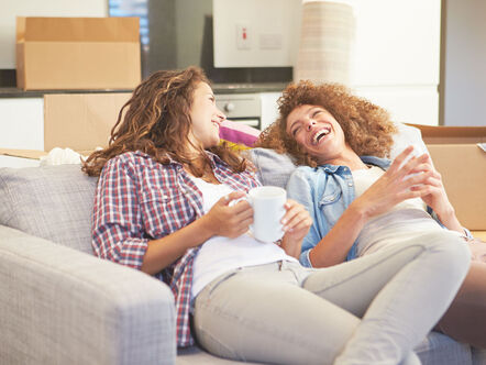 Two Women Relaxing On Sofa With Hot Drink In New Home